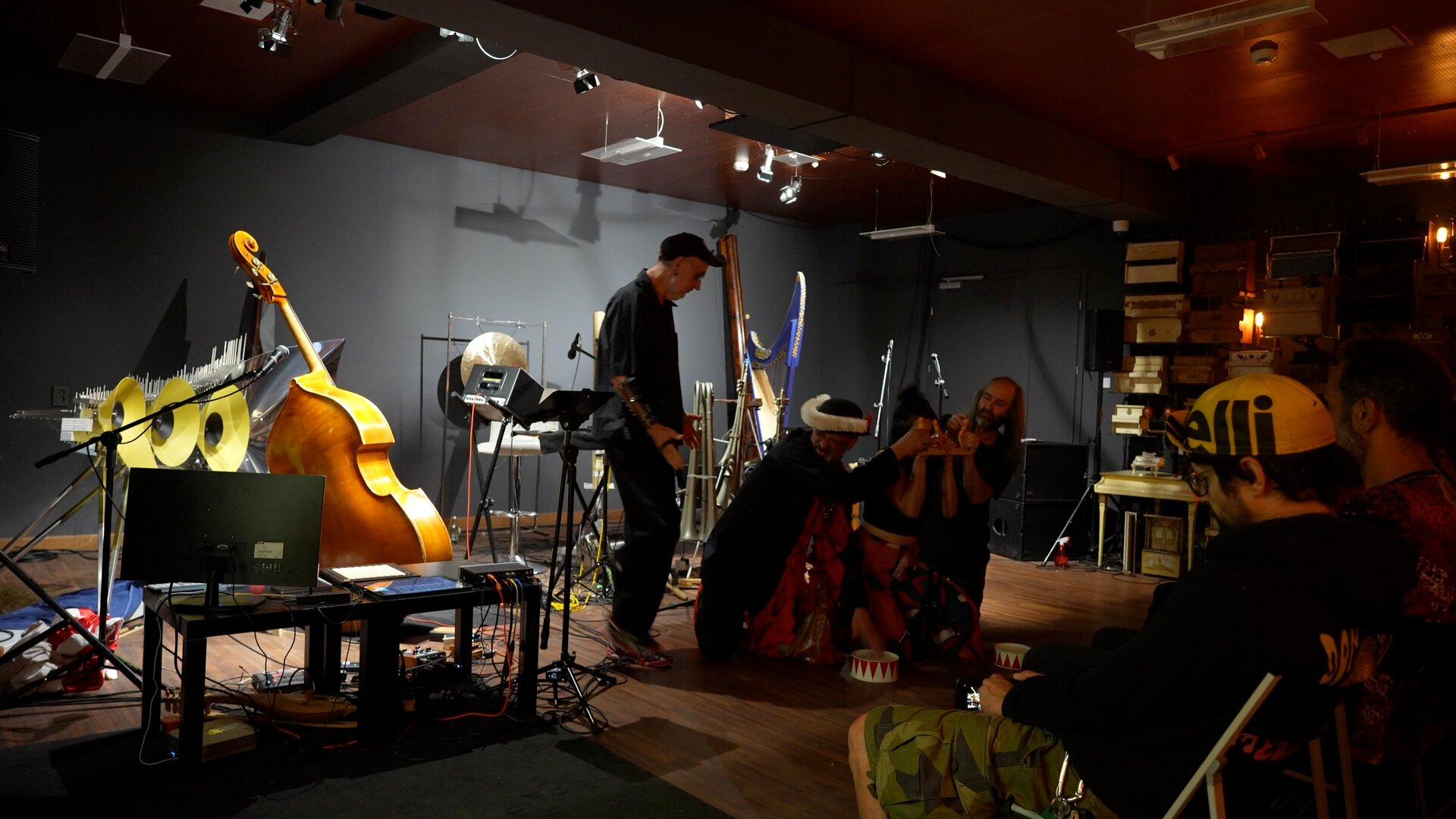 Wide view of KATÁBASIS: performers, the double bass and numerous instruments on stage, with audience members visible on the right.